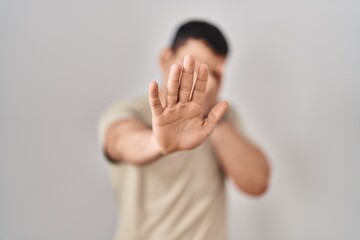 Young arab man wearing casual t shirt covering eyes with hands and doing stop gesture with sad and...