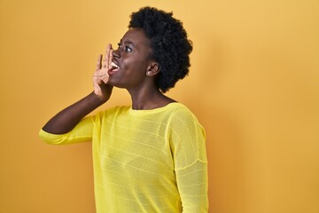 African young woman standing over yellow studio shouting and screaming loud to side with hand on mouth. communication concept.