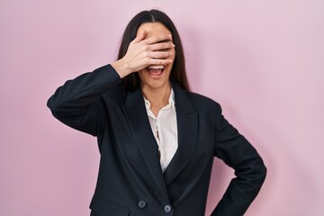 Young brunette woman wearing business style over pink background smiling and laughing with hand on face covering eyes for surprise. blind concept.