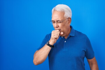 Middle age man with grey hair standing over blue background feeling unwell and coughing as symptom for cold or bronchitis. health care concept.