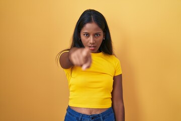 Young indian woman standing over yellow background pointing displeased and frustrated to the...
