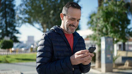Middle age man smiling confident using smartphone at park