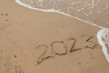 Happy New Year 2023, lettering on the beach with wave and clear blue sea. 