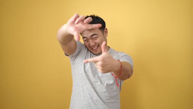 Young chinese man smiling confident doing photo gesture with hands over isolated yellow background