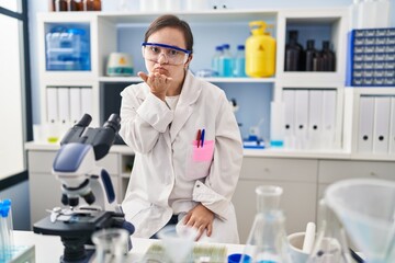 Hispanic girl with down syndrome working at scientist laboratory looking at the camera blowing a kiss with hand on air being lovely and sexy. love expression.