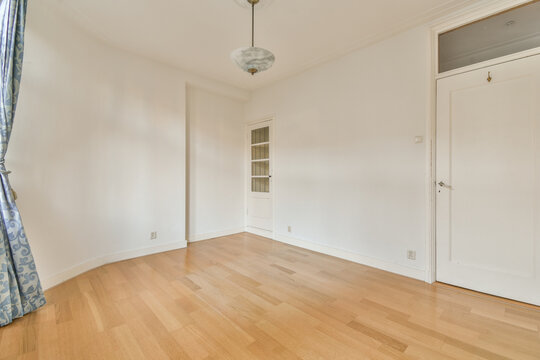 An Empty Room With Wood Floors And White Walls, There Is A Light Blue Curtain Hanging From The Window Above