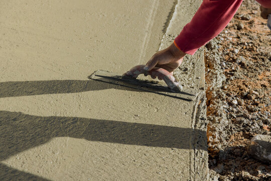 Using trowel worker plasters wet concrete cement floor after concrete has been poured