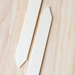 two wooden sticks with pointed ends (gardening sticks used to identify plants) on a wooden surface