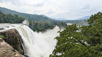 Fototapeta premium a mystical white waterfall at the center of a dark green forest surrounded by hills and mountains in the summer