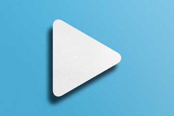 White paper cut into triangle shape, play button set on light blue paper background.