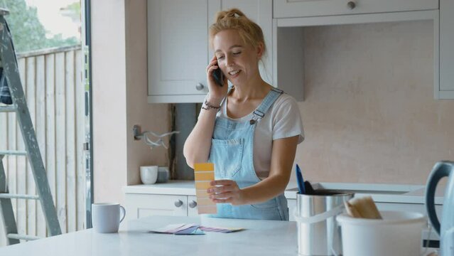 Woman renovating kitchen at home looking at paint colour swatches and talking on mobile phone - shot in slow motion