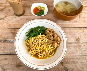 Noodle chicken soup (mie ayam) with vegetable, broth, and iced coffee. Indonesia food served on bowl.