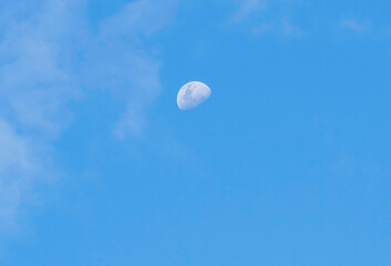 Late afternoon partial moon rising amongst the soft high cloud in the blue sky