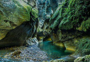 The turquoise water of the river flowing the lichen and moss covered chasm walls in the beautiful ...