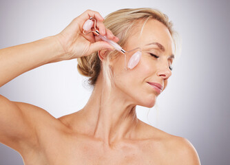 Woman, roller and skincare for cosmetics, anti aging or facial treatment against a gray studio...