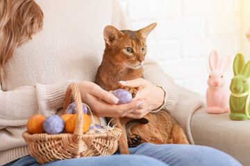 Woman with cute Abyssinian cat and basket of Easter eggs at home