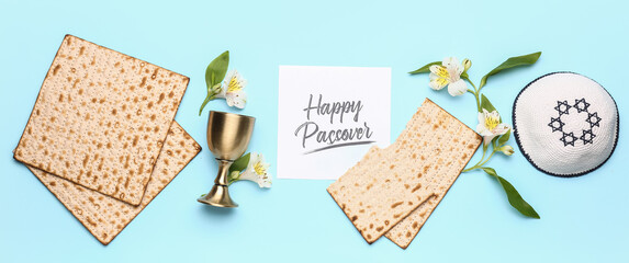 Jewish flatbread matza for Passover, flowers, greeting card, kippah and goblet on light blue background