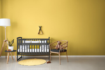 Interior of modern nursery with stylish baby crib, lamp, table and armchair