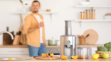 Modern juicer with cut fresh oranges on table in kitchen