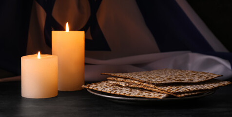 Burning candles, matzo flatbread and flag of Israel on dark background
