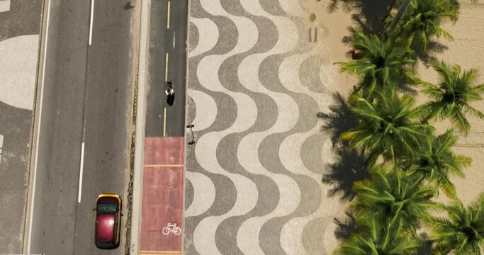 Overhead Aerial View Of Famous Boardwalk On Copacabana Beach With Palm Trees And People Riding Bicycles, Rio De Janeiro, Brazil