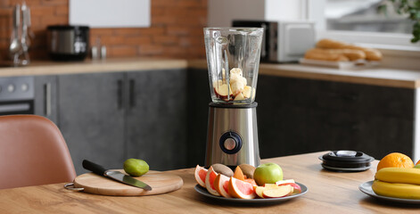 Modern blender with fresh fruits and cutting board on table in kitchen
