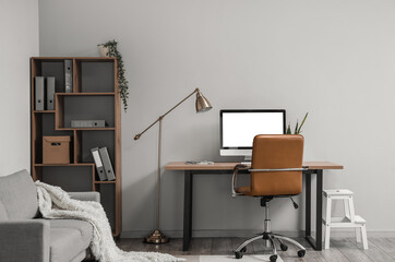 Interior of light office with table, modern computer and shelving unit