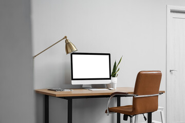 Modern table with computer and chair near light wall