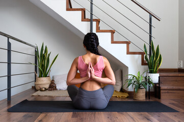 Rear view of woman doing reverse prayer yoga pose at home living room. Female yogi doing namaste...