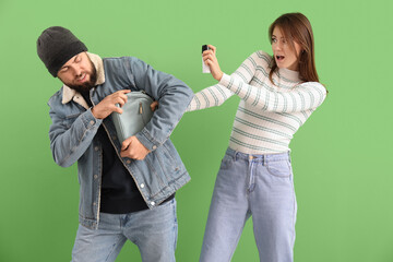 Young woman with pepper spray defending herself against thief on green background
