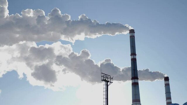 Global warming problem. White smoke from chimney of thermal power stationboiler room, thermal power plant, white smoke against a blue sky, sun behind clouds of smog. very cold. 4k