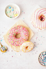 Parchments with different delicious donuts and bowls of sprinkles on white table