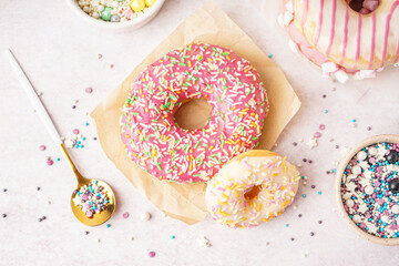 Parchments with different delicious donuts and bowls of sprinkles on white table