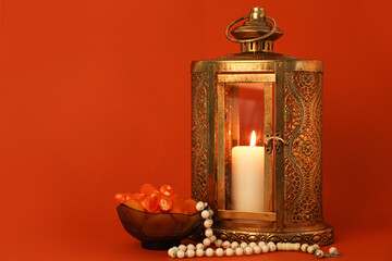 Muslim lantern with burning candle, dates and tasbih for Ramadan on color background
