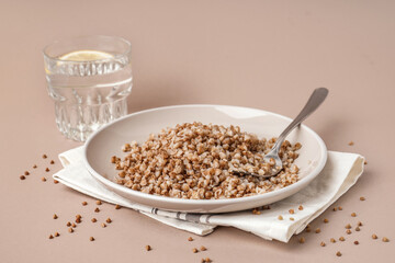 Napkin with plate of tasty buckwheat porridge and glass of water with lemon on beige background