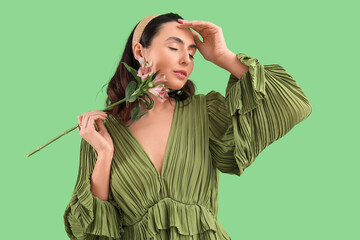 Young woman in dress with alstroemeria flowers on green background