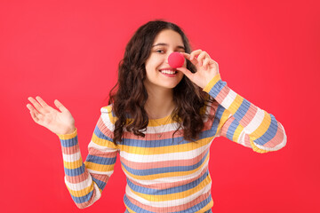 Teenage girl with clown nose on red background. April Fools' Day celebration