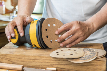 Carpenter attach sandpaper to an orbital sander or palm sander after remove the paper backing of the sandpaper.DIY maker and woodworking concept. selective focus