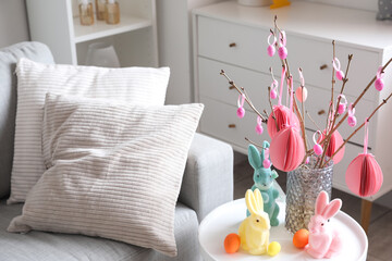 Vase with tree branches, Easter eggs and rabbits on table in living room