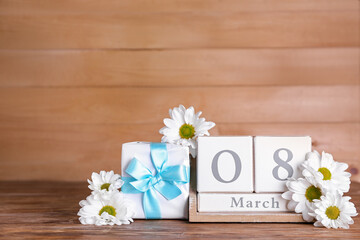 Cube calendar with date MARCH 8, gift box and beautiful chamomile flowers on wooden table. Women's Day celebration