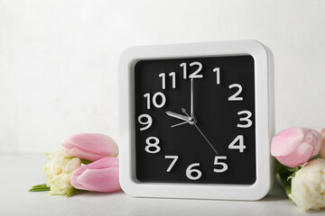 Alarm clock and beautiful tulip flowers on light background