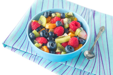 In a glass bowl, fresh fruit salad with raspberries, blueberries, slices of kiwi, apples, tangerines, grapes.White background.