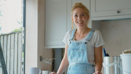 Portrait of smiling woman wearing dungarees renovating kitchen at home - shot in slow motion
