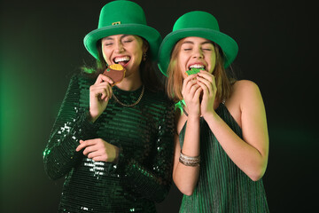 Young women in hats eating cookies on dark background. St. Patrick's Day celebration