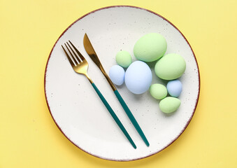 Table setting with Easter eggs and cutlery on yellow background