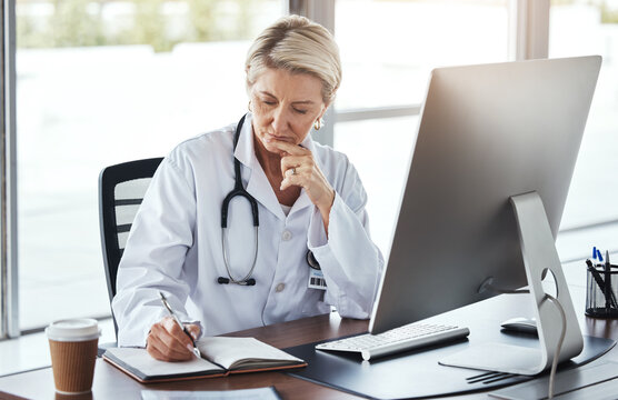 Senior Woman, Doctor And Writing In Book By Office Desk For Healthcare Research, Notes Or Planning. Elderly Female Medical Professional Thinking With Notebook By Computer For Health Strategy Or Plan