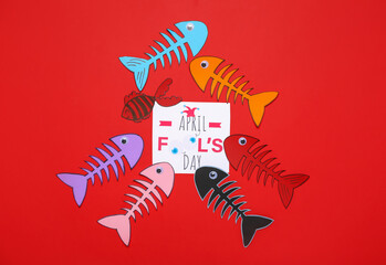 Card with text APRIL FOOL'S DAY and paper fish skeletons on red background