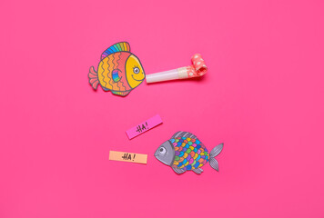 Composition with paper fishes, words HA and whistle on pink background. April Fool's Day celebration