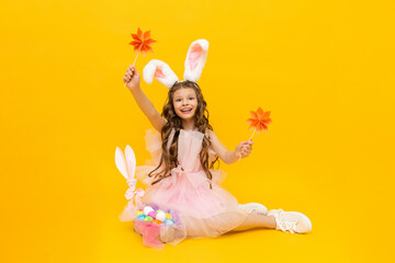 Festive Easter.  A happy little girl is sitting and enjoying the spring holiday. A child with rabbit ears on a yellow isolated background.