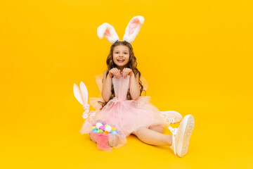 Festive Easter. A little girl depicts an Easter bunny with a basket of colorful eggs. A child with rabbit ears on a yellow isolated background